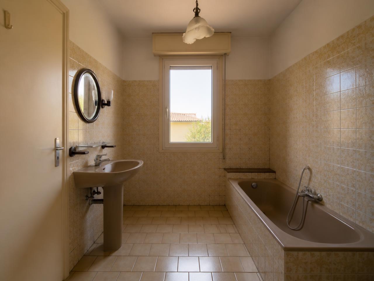 Salle de bain vétuste avant travaux : carrelage beige daté, baignoire ancienne et joints abîmés