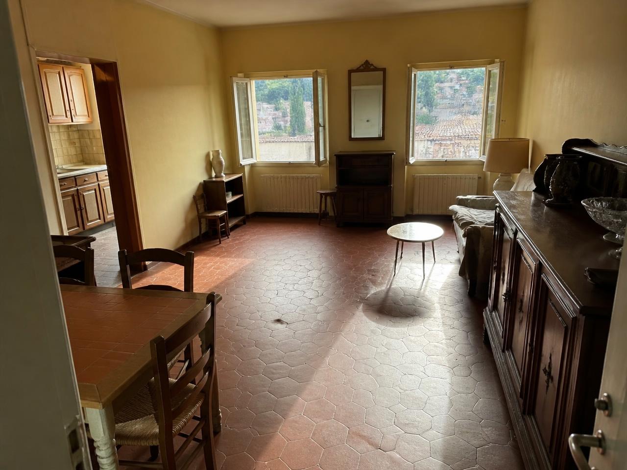 Séjour et cuisine d'un appartement avant rénovation : sol en tomettes brunes et meubles anciens